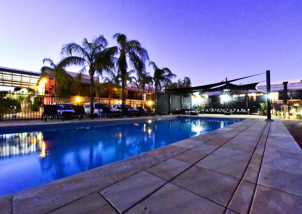 a swimming pool with palm trees in front of a building at Diplomat Hotel Alice Springs in Alice Springs