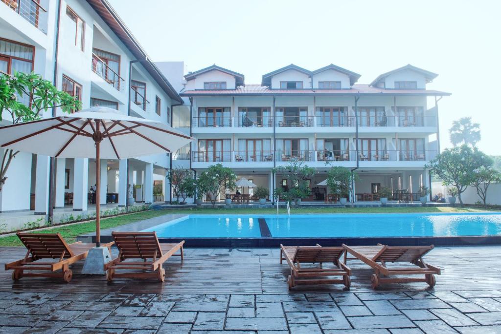 a pool with chairs and an umbrella next to a building at Cardamon Hotel Nilaveli in Nilaveli