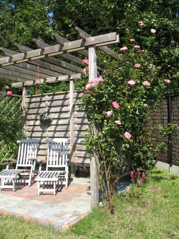 a wooden pergola with two chairs and a bush with pink roses at B&Logies De Duinroos Koksijde in Koksijde