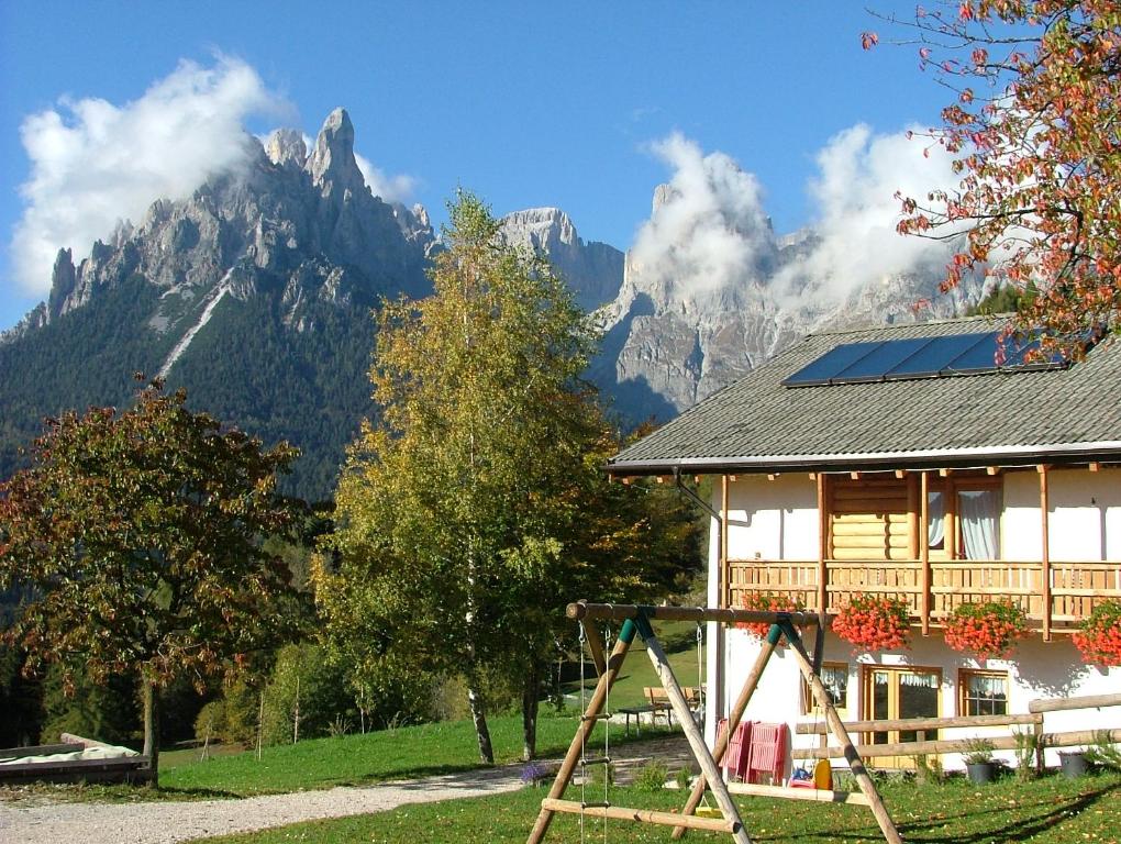 uma casa com um parque infantil em frente a uma montanha em Agritur Dalaip dei Pape em Fiera di Primiero