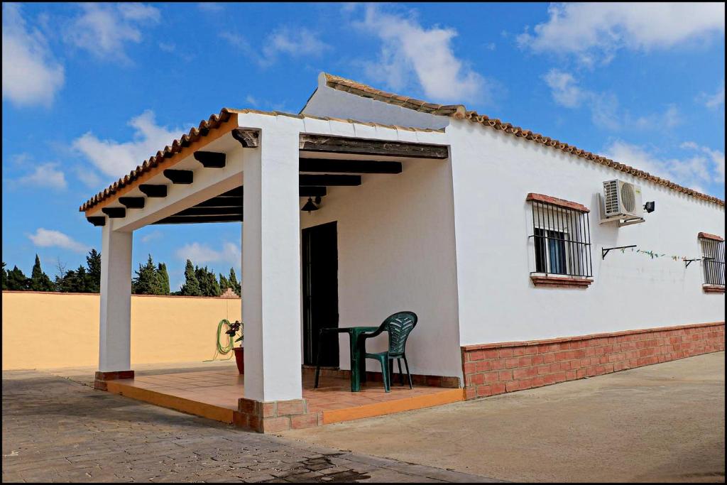 Una pequeña casa blanca con una silla en un porche. en Bungalow en complejo I, en Conil de la Frontera