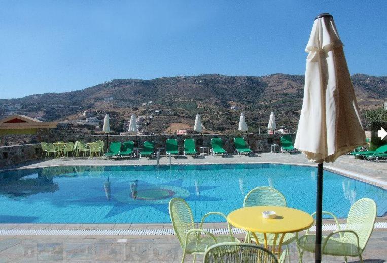 a pool with a yellow table and chairs and an umbrella at Perla Apartments in Agia Pelagia