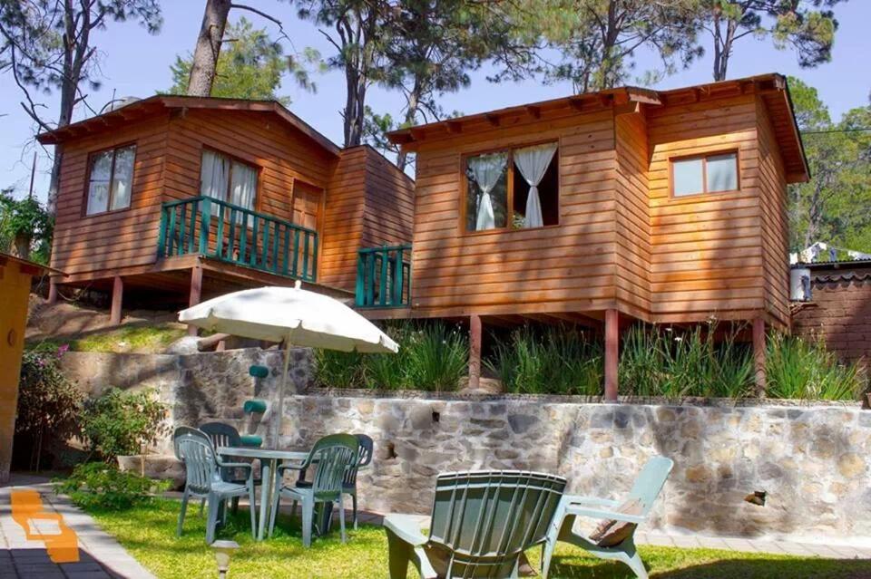 ein Holzhaus mit einem Tisch, Stühlen und einem Sonnenschirm in der Unterkunft Cabañas Monte Alto Hotel Boutique in Valle de Bravo