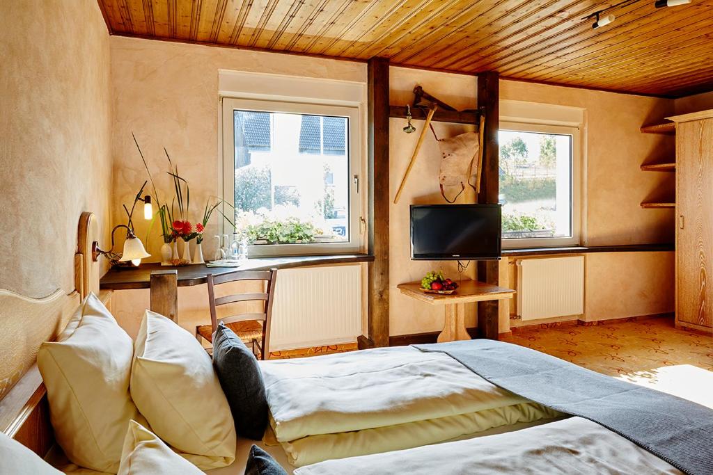 a bedroom with a bed and a tv and two windows at Steinbergs Wildewiese NaturHotel in Wildewiese