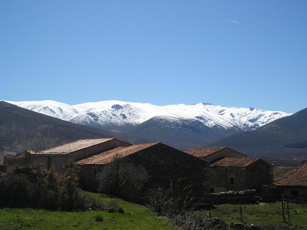 un grupo de edificios con montañas cubiertas de nieve en el fondo en El Tormal, en Navalonguilla