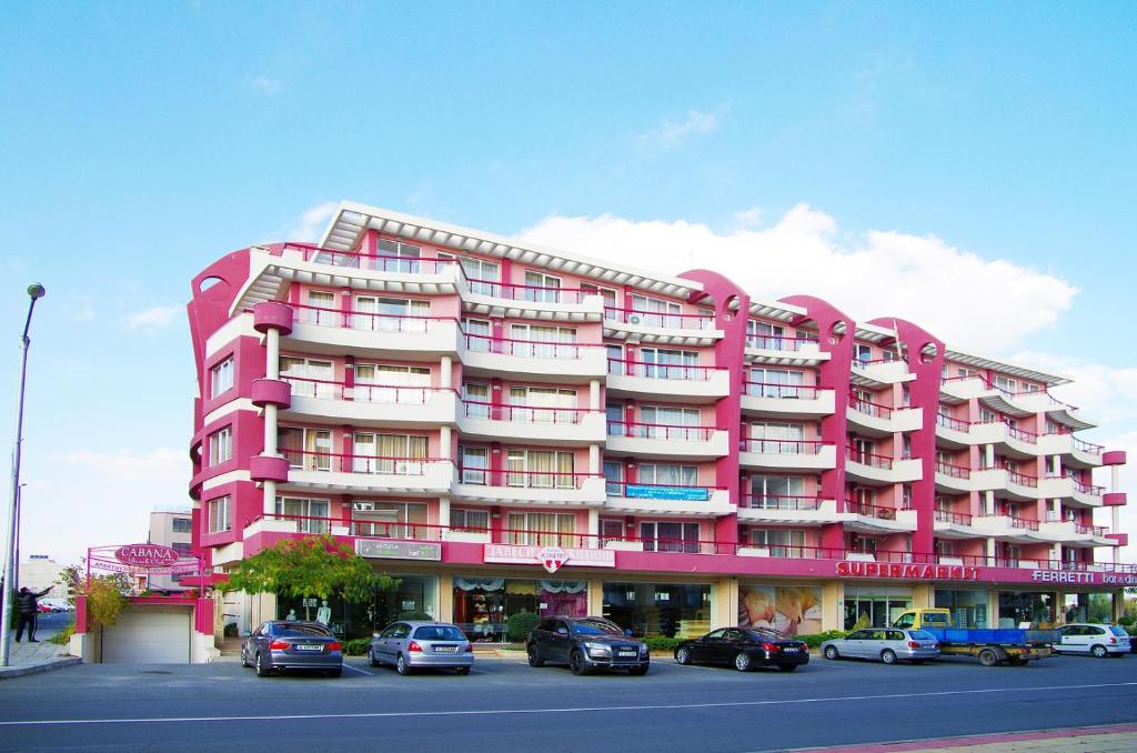 een roze gebouw met auto's geparkeerd op een parkeerplaats bij Cabana Beach Club Complex in Nesebar