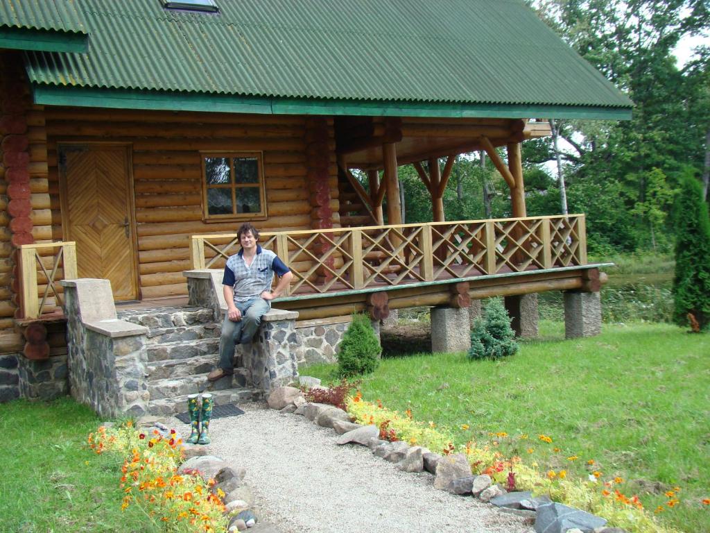 a man sitting on a stone wall in front of a cabin at Vecskrīveri in Dundaga
