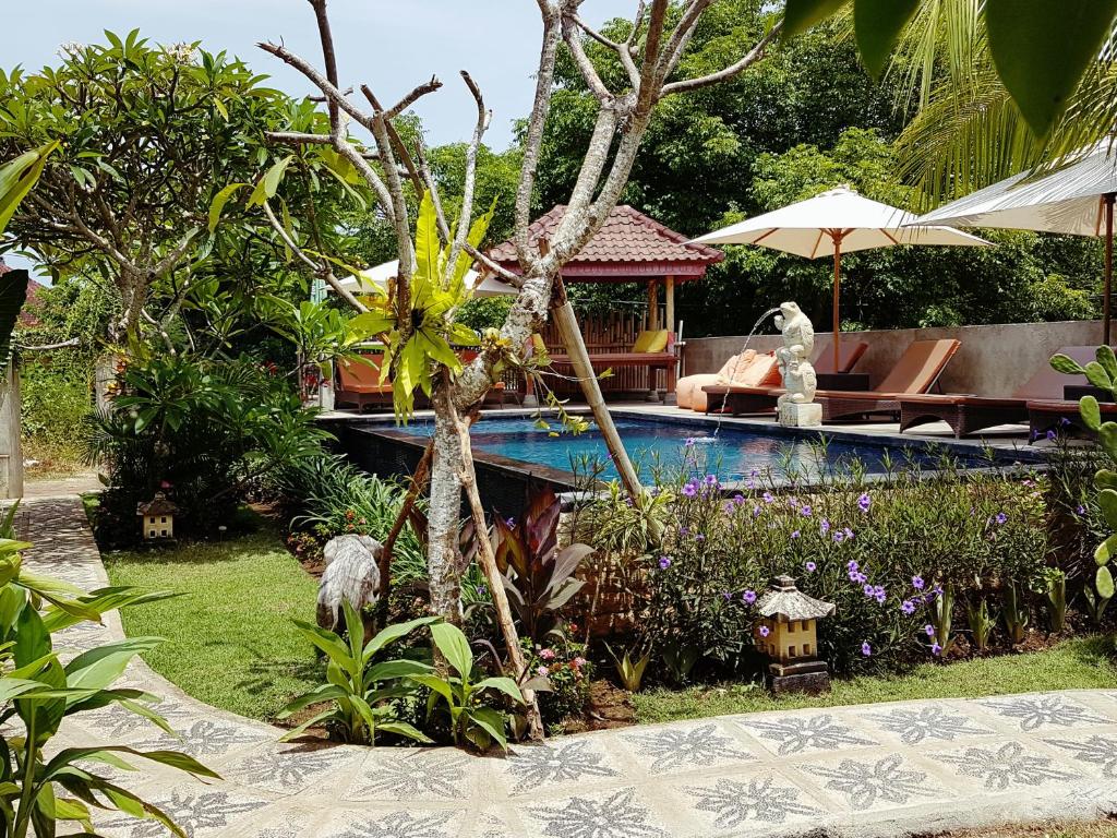 a pool in a garden with a bench and umbrella at The Akah Cottage in Nusa Lembongan