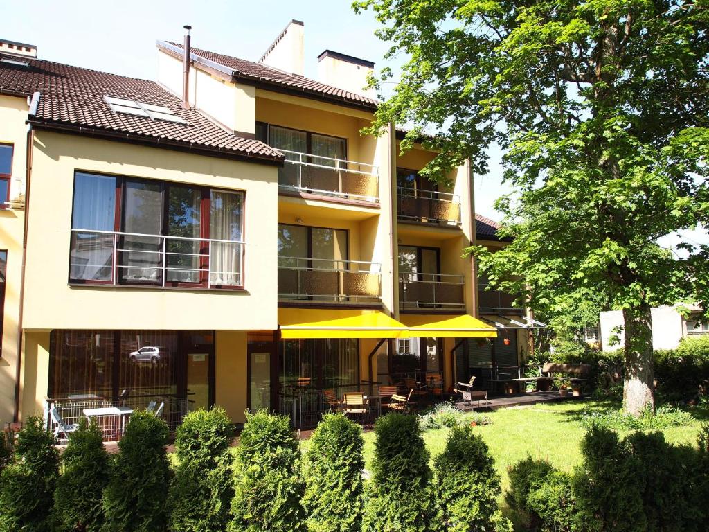 un bâtiment jaune avec une terrasse et un arbre dans l'établissement Pušynas Apartments, à Juodkrantė
