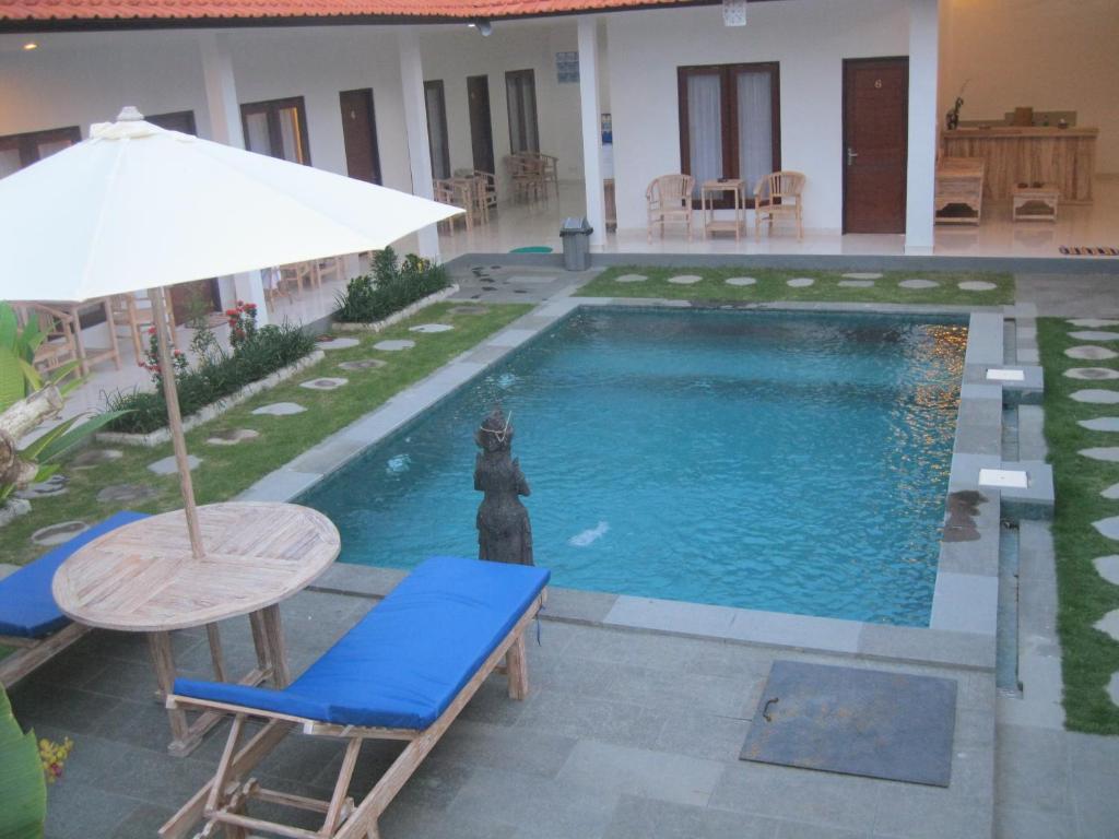 a pool with a cat statue next to a table and an umbrella at Temuku Guest House in Canggu