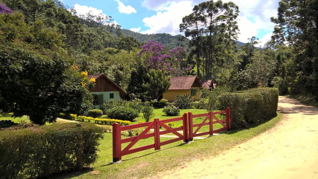 een rood hek in een tuin met een huis op de achtergrond bij Pousada Sítio das Astrapéias in Visconde De Maua