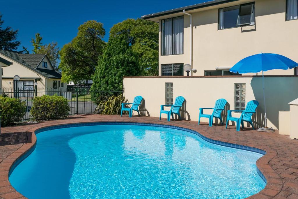 a swimming pool with chairs and a table and umbrella at Ashleigh Court Motel in Blenheim