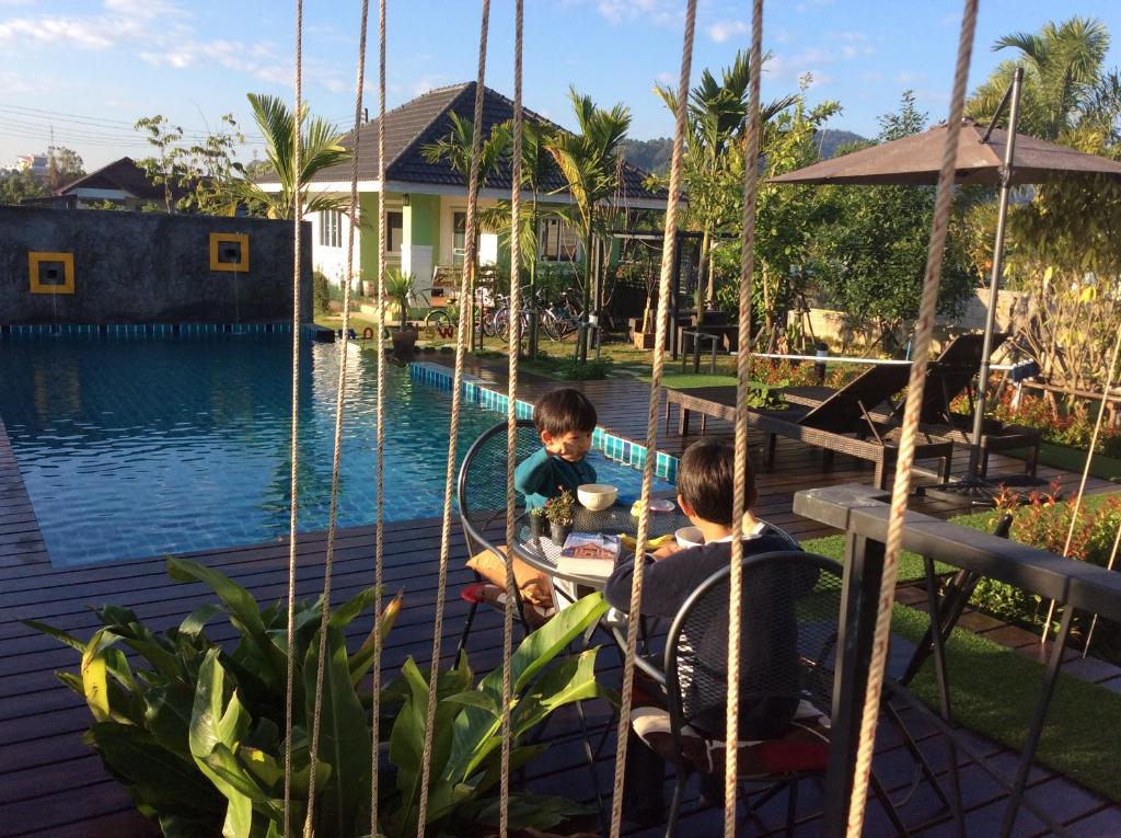 twee kinderen zitten aan een tafel op een schommel aan het water bij Na Na Doo Homestay in Chiang Rai