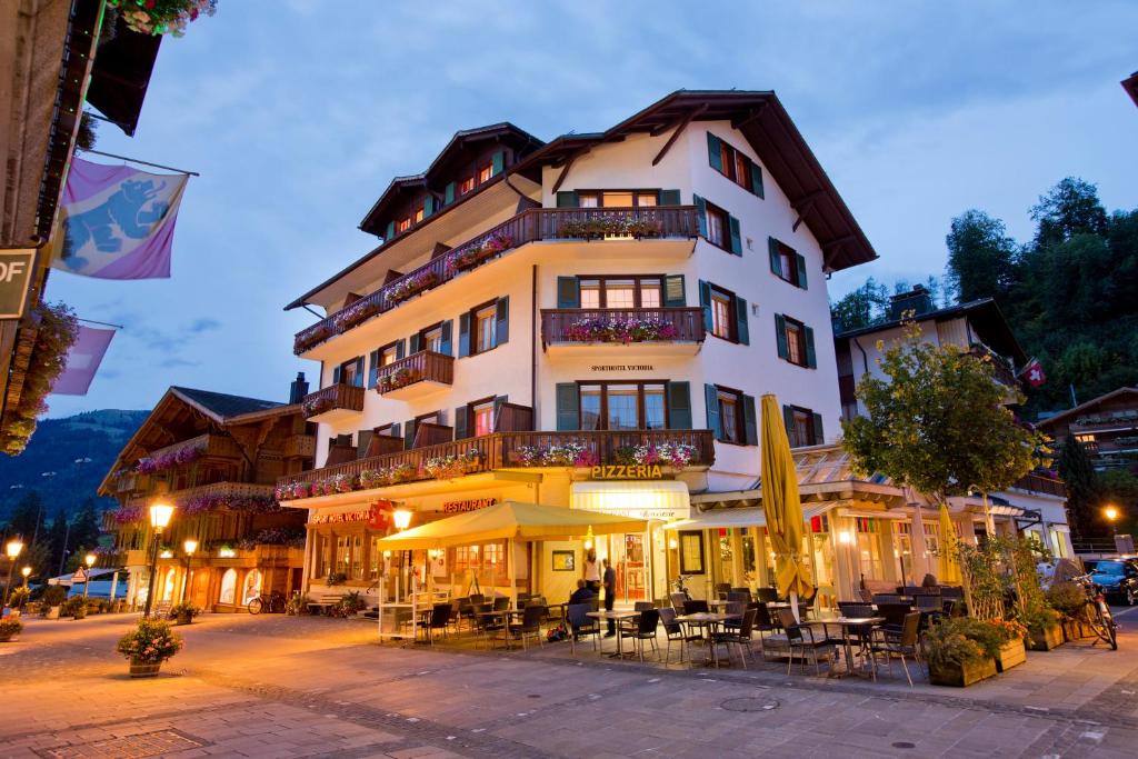 ein großes Gebäude mit Tischen und Stühlen davor in der Unterkunft Sporthotel Victoria in Gstaad