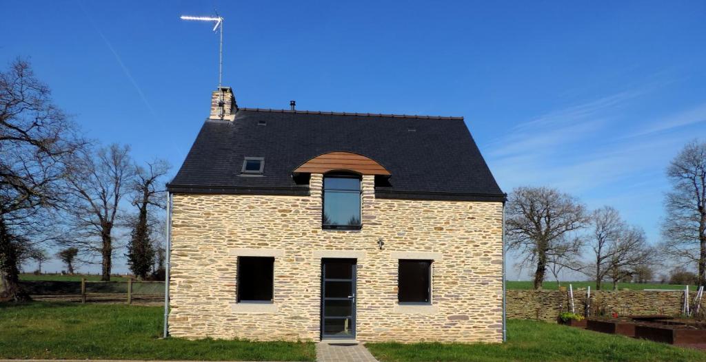 Campénéac的住宿－薩福克爾度假屋，一块砖砌的房子,在田野上有一个黑色的屋顶