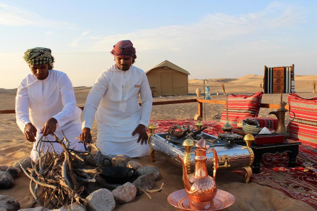 dos hombres parados junto a un fuego en el desierto en Legend Desert camp, en Fulayj al Mashāʼikh