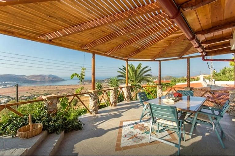 een patio met een tafel en stoelen en uitzicht op het strand bij Nadia's Traditional Greek House in Anavissos