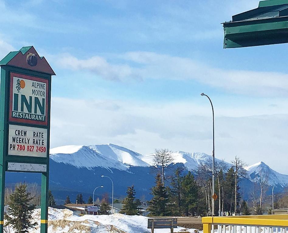 una señal para una posada con montañas en el fondo en Alpine Lodge Motel & Restaurant, en Grande Cache