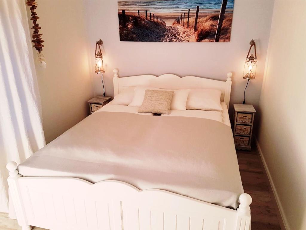 a white bed in a bedroom with two lamps at Strandgut - das appartement in Schönhagen