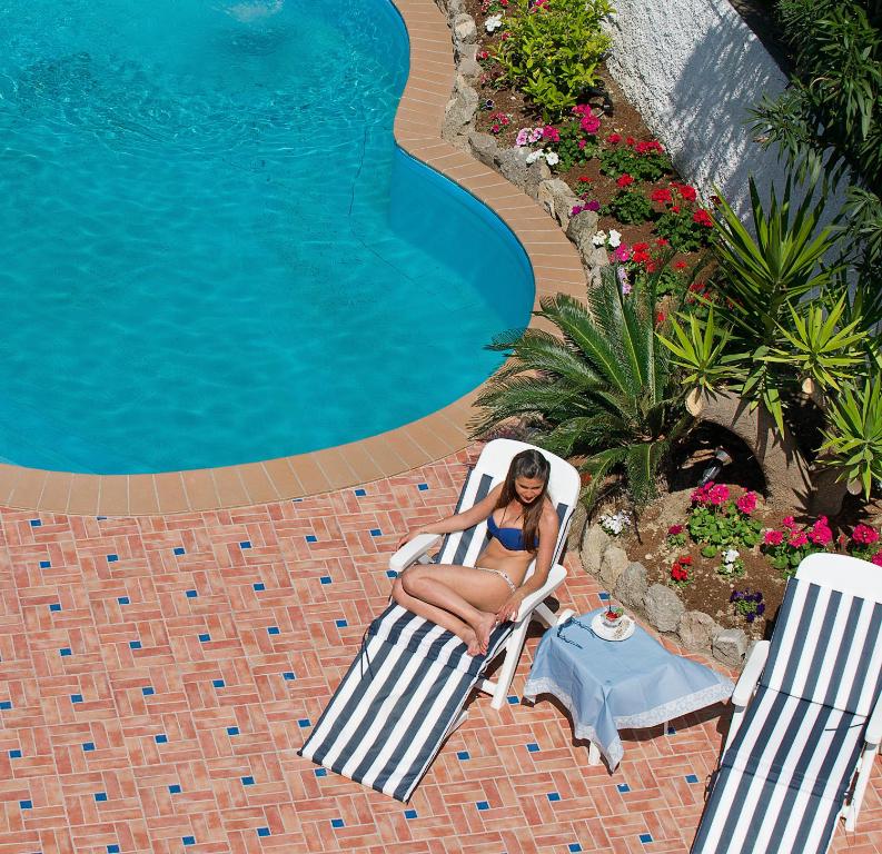 a woman sitting in a chair next to a swimming pool at Iris Hotel in Ischia