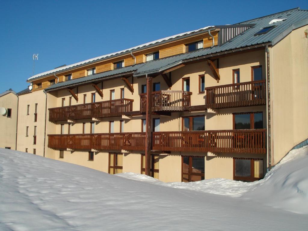 un grand bâtiment avec de la neige devant lui dans l'établissement Village Vacances Passion Georges Moustaki, à Les Moussières