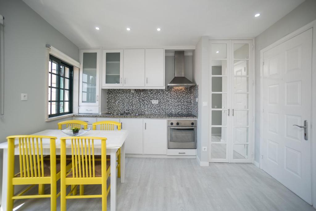 a white kitchen with yellow chairs and a table at Apartamento Casa Amarela in Sesimbra