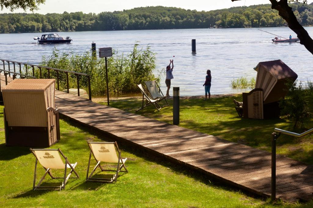 a woman standing on a dock with two chairs and a person fishing at Seminaris SeeHotel Potsdam in Potsdam