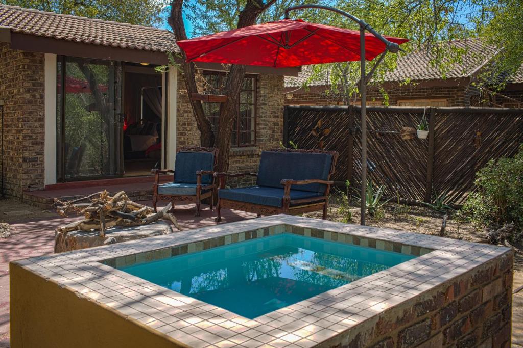 a swimming pool with an umbrella and two chairs and a house at Manzini Cottage in Marloth Park