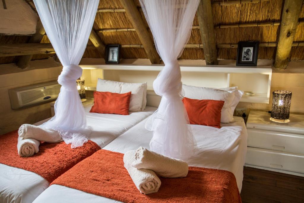 two beds in a room with white curtains and towels at Majuli River House in Marloth Park