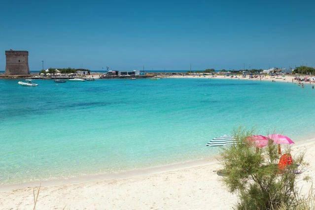 una spiaggia con acqua blu e ombrelloni rosa di Casa Vacanze Sole e Mare a Porto Cesareo