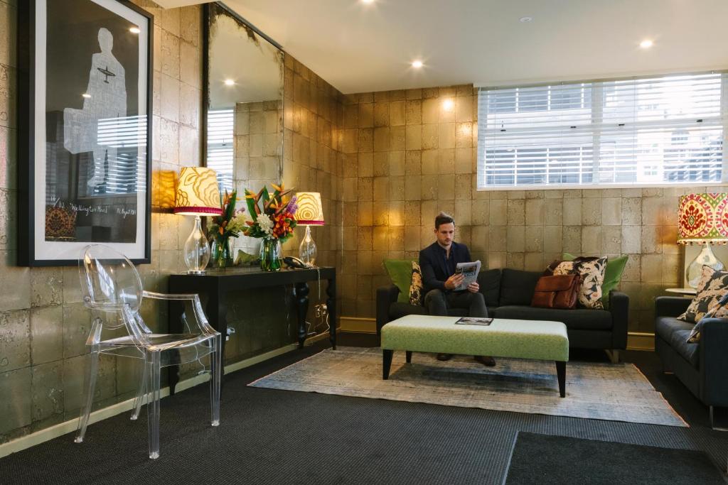 un hombre sentado en un sofá en una sala de estar en Gilmer Apartment Hotel, en Wellington