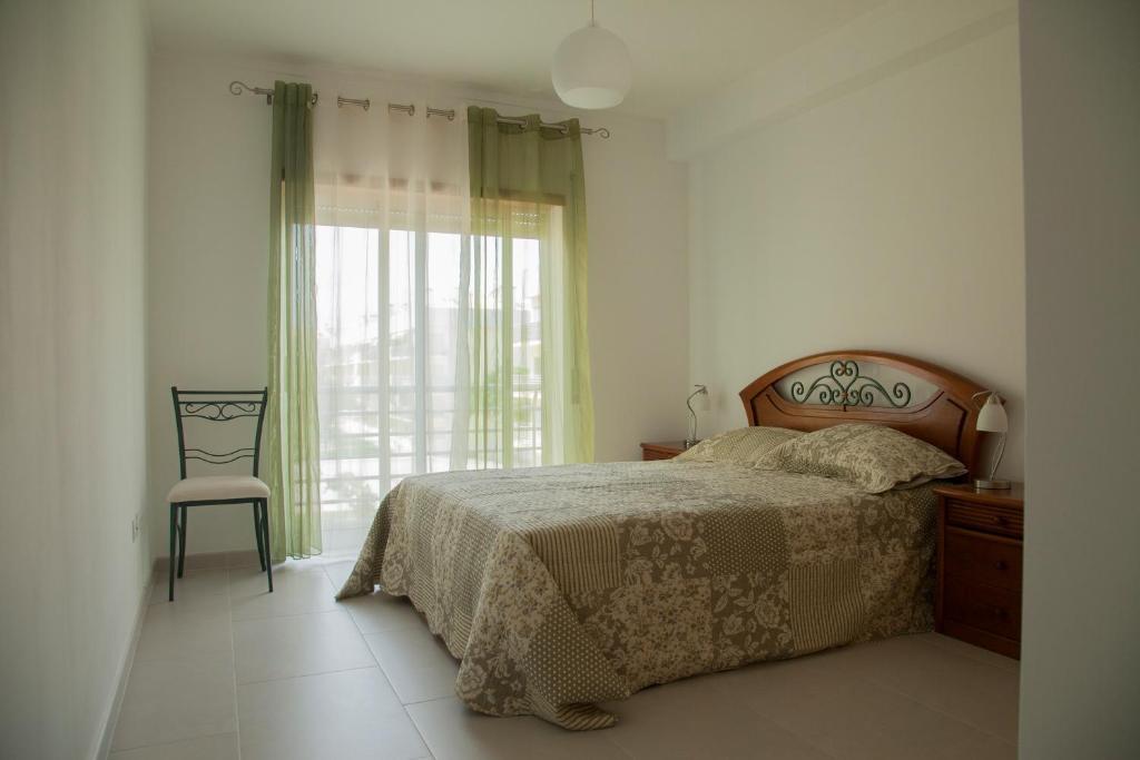 a bedroom with a bed and a chair and a window at Apartamento Urbanização Aurora Rio in Vila Real de Santo António