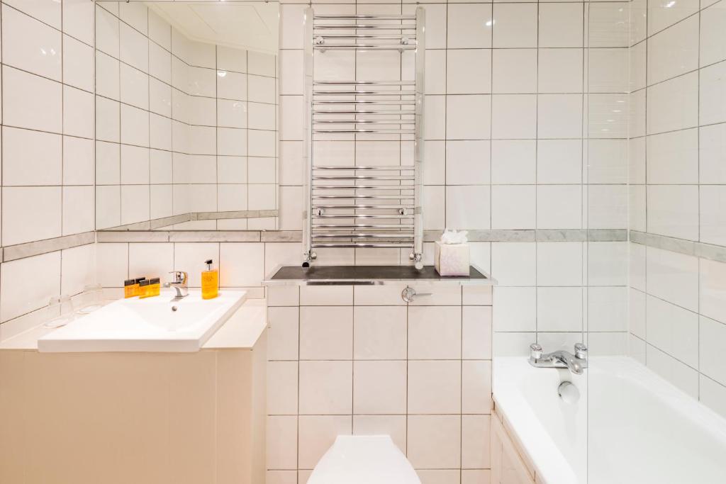 a white tiled bathroom with a sink and a tub at The California - London Kings Cross in London