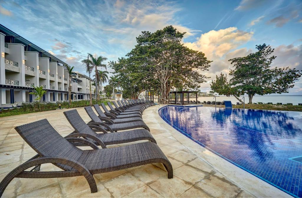 a row of chaise lounge chairs next to a swimming pool at Royalton Negril, An Autograph Collection All-Inclusive Resort in Negril