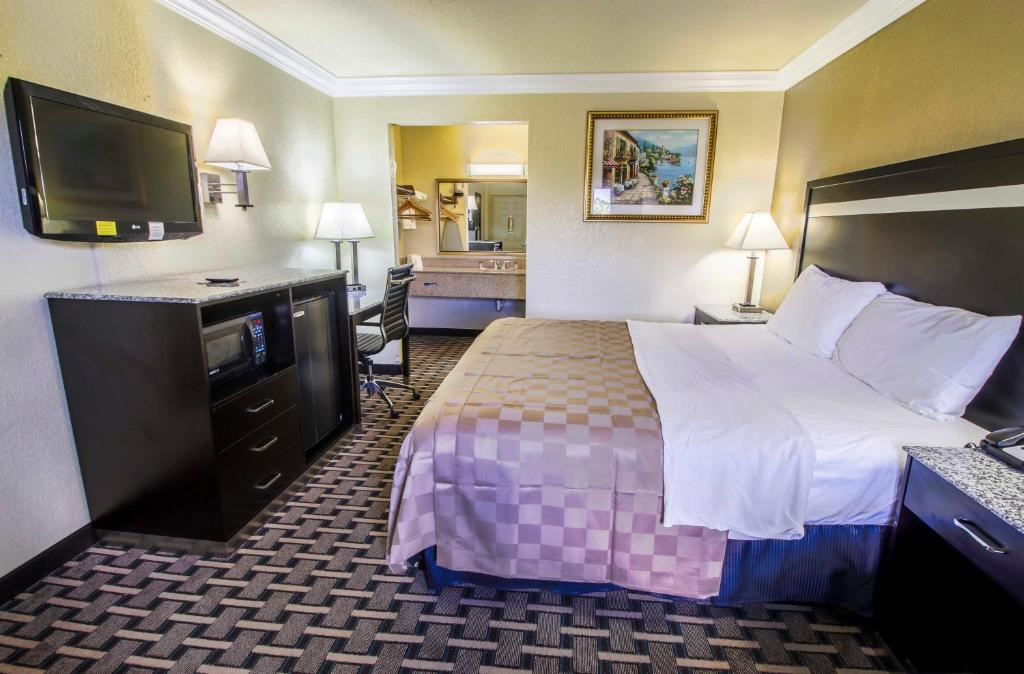 a hotel room with a bed and a flat screen tv at Inn of America in Palm Beach Gardens