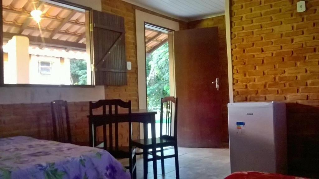 Habitación con mesa, sillas y nevera. en Chales Jeitinho Mineiro, en São Thomé das Letras