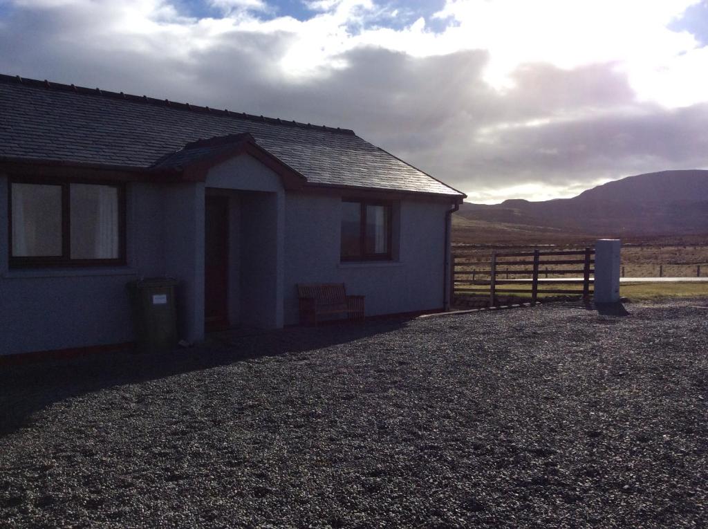 una pequeña casa blanca con una valla y montañas al fondo en Buaile nan Carn, en Kilmuir