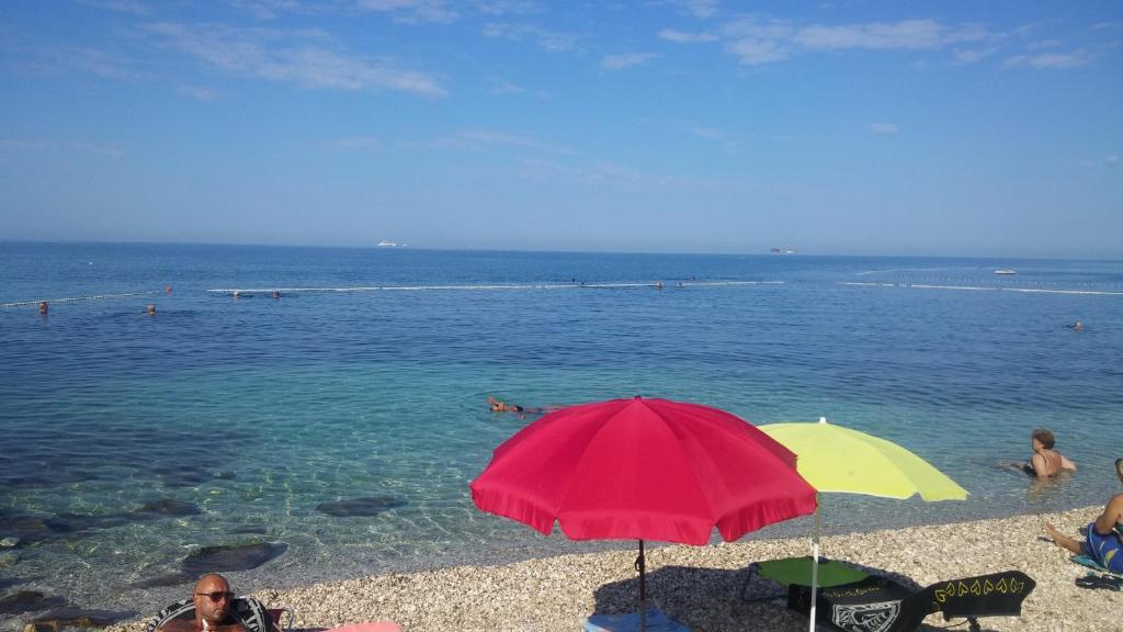 a red and yellow umbrella on a beach with people in the water at Apartments Timi in Poreč