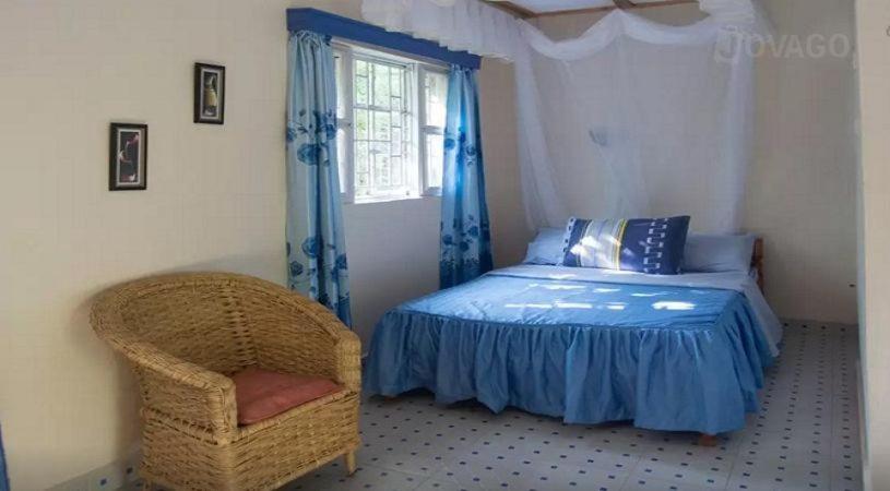 a bedroom with a bed and a chair and a window at Ose Cottages in Kisumu