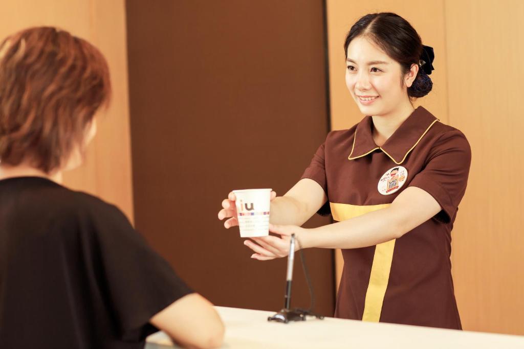 a woman is holding a cup in front of a mirror at IU Hotel Hezhou Bus Terminal in Hezhou