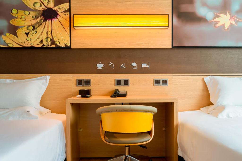 a desk with a yellow chair in a room with two beds at IU Hotel Hezhou Bus Terminal in Hezhou