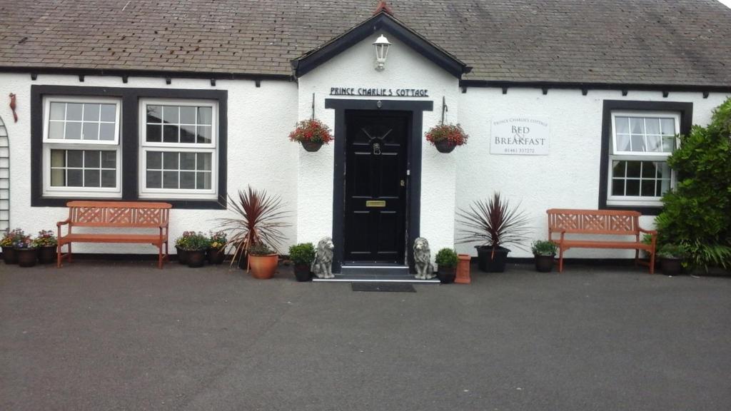 a white building with two benches in front of it at Prince Charlie's Cottage in Gretna Green