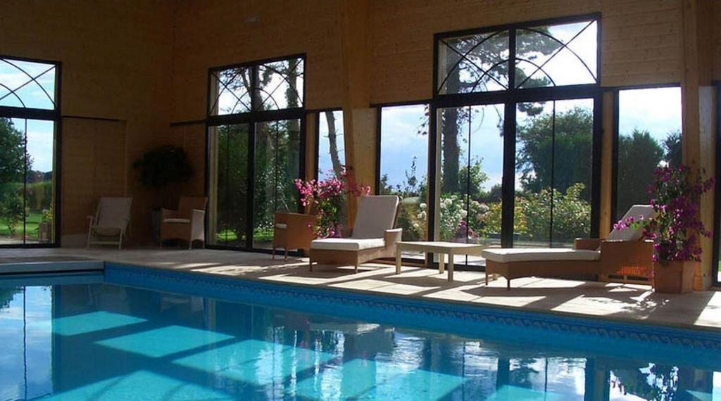 una piscina con sillas, una mesa y ventanas en Nature et Lin, en Néville