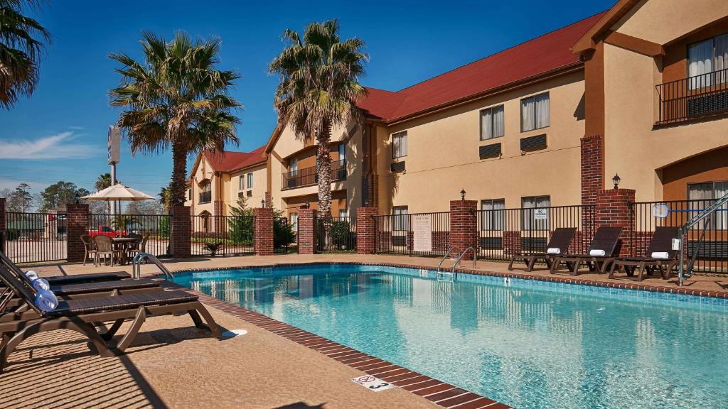 a swimming pool in front of a building with palm trees at Best Western Bayou Inn and Suites in Lake Charles