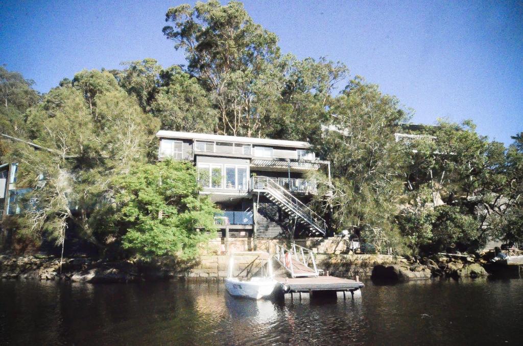 a house on the river with a boat in the water at Calabash Bay Lodge in Berowra