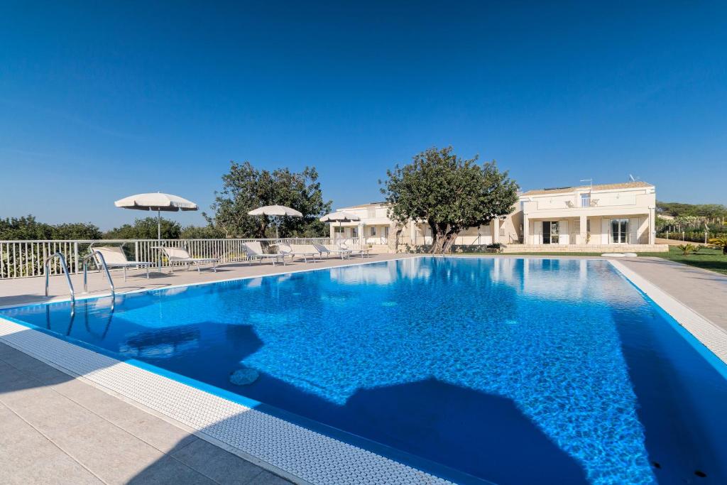 a large blue swimming pool with chairs and umbrellas at Il Giardino dei Frangipani in Santa Croce Camerina