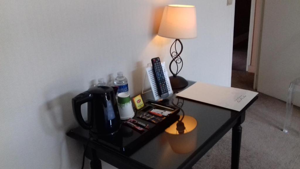 a table with a coffee maker and a lamp on it at Logis Hôtel-Restaurant Les Airelles in Neufchâtel-en-Bray