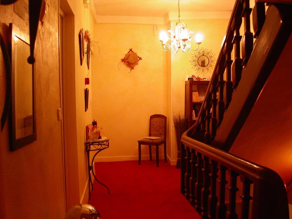a hallway with a staircase and a chair and a chandelier at Hôtel le Dauphin in Moulins-la-Marche