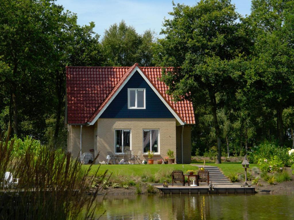 een huis met een rood dak naast een meer bij Spacious holiday home with a dishwasher, 20 km. from Assen in Westerbork