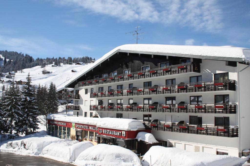śnieżny budynek z pociągiem przed nim w obiekcie Sporthotel Walliser w mieście Hirschegg